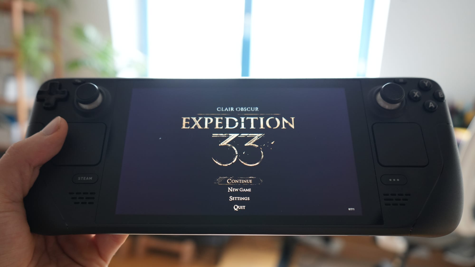 Steam Deck Handheld-Konsole zeigt den Startbildschirm von Clair Obscur: Expedition 33 in einer Wohnzimmer-Umgebung