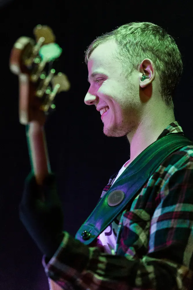 Weißer Mann in Karo Hemd spielt E-Bass bei einem Auftritt